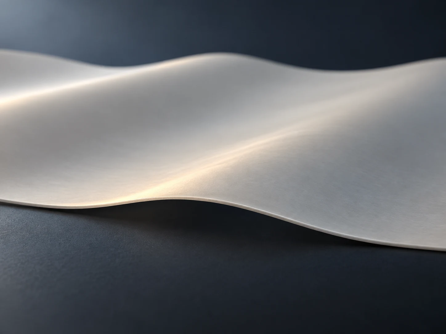 Conceptual image of a pale grey-white material rolled into a thin even film curving gently on a dark surface