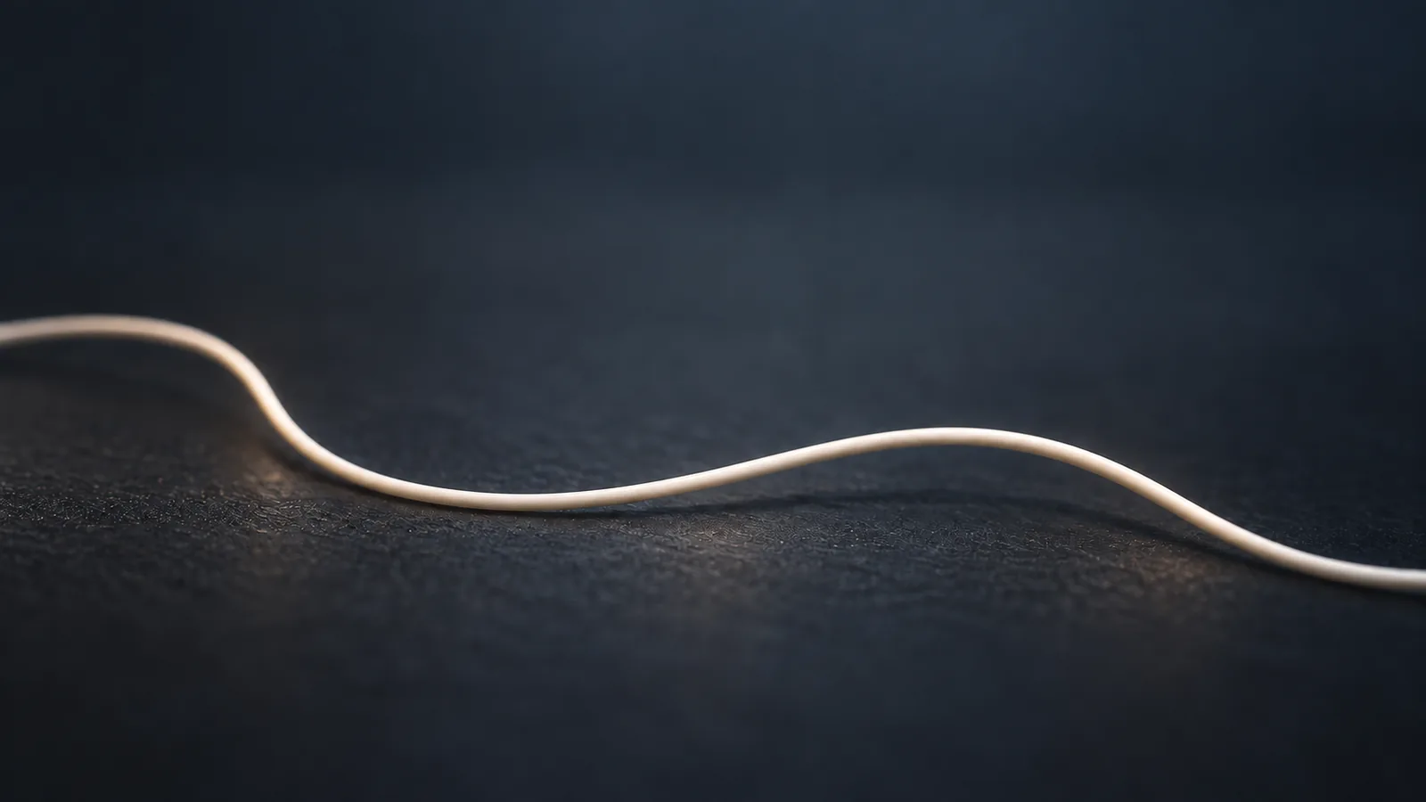 Abstract conceptual image of a single thin, smooth thread lying in a gentle curve on a dark surface