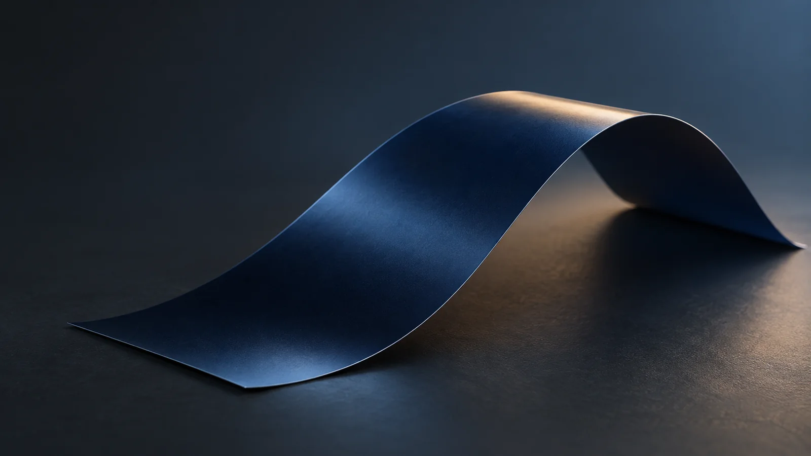 Conceptual image of a single thin, plain dark film lying in a gentle arc against a dark background, with soft light flowing across its surface